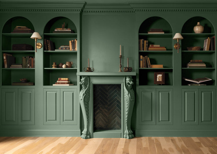 A green painted room with lower paneled walls and arched, built-in shelving topped with books and decor.